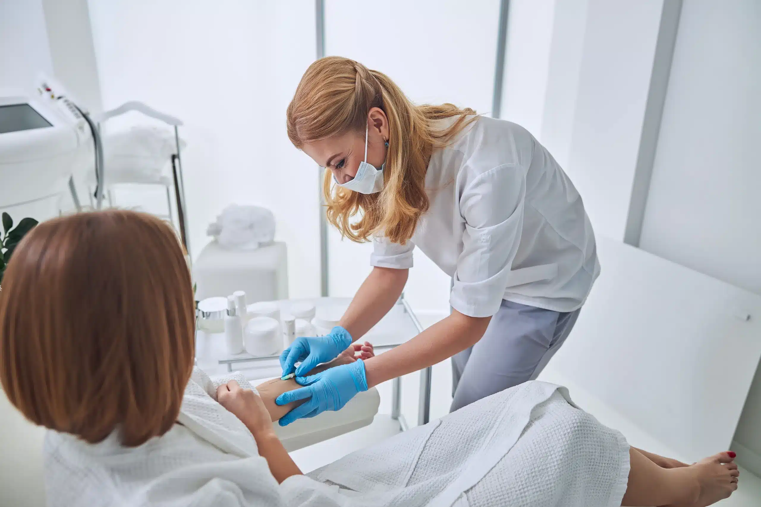 Licensed nurse in a modern wellness clinic is administering IV vitamin therapy to a relaxed female patient wearing a spa robe at Seashore MD in Little Silver, NJ.